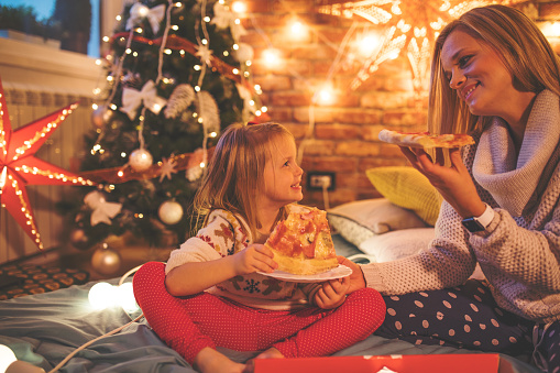 Mother and daughter eating pizza in front of Christmas tree