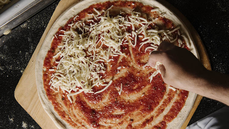 Pizza maker sprinkling shredded cheese on a pizza