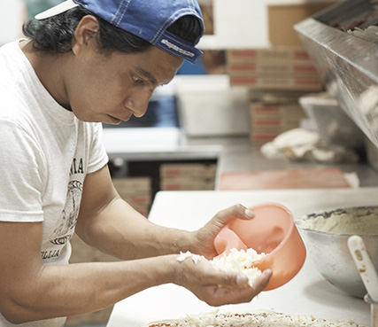 Pizza operator portioning Grande cheese on a pizza