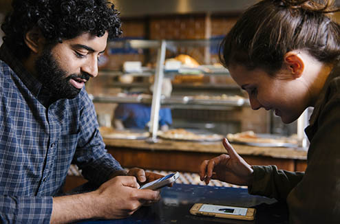 Man and woman looking at pizzeria website on their phones while sitting at a pizzeria